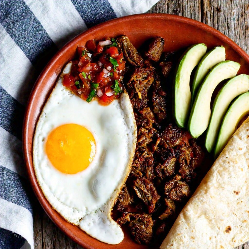 A hearty plate of carnitas and eggs with garnishes.