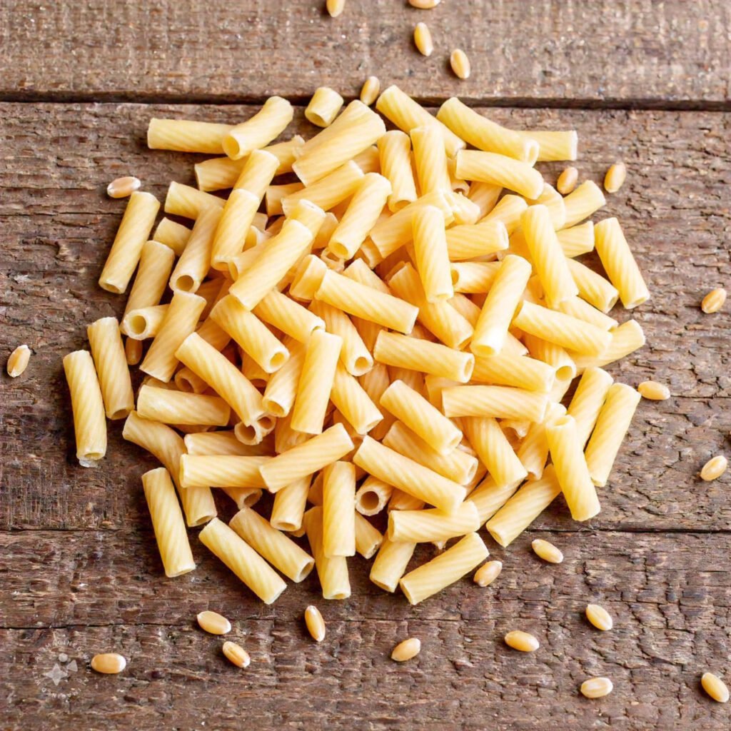 A detailed close-up of uncooked ditalini pasta on a rustic wooden table, with soft natural lighting and scattered grains of durum wheat for added texture.