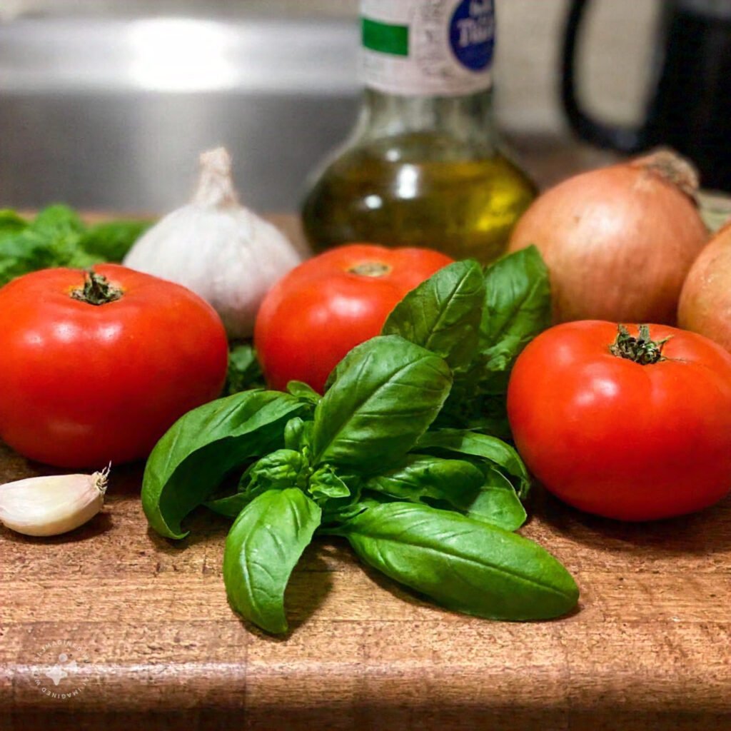 Fresh tomatoes, basil, garlic, onions, and olive oil on a rustic wooden countertop