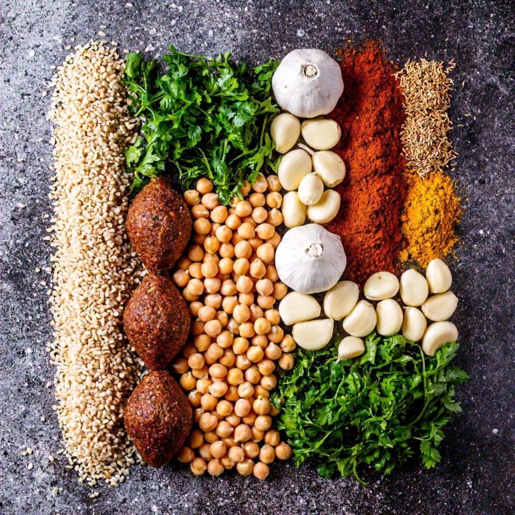 Ingredients for kibbeh and falafel, including bulgur, chickpeas, spices, and fresh herbs, arranged on a table.