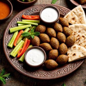 What Is the Difference Between Kibbeh and Falafel? 1 A platter with golden kibbeh and falafel served with yogurt, tahini sauce, and fresh vegetables.