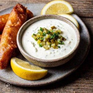 A bowl of homemade tartar sauce placed next to crispy fish and chips on a rustic wooden table.